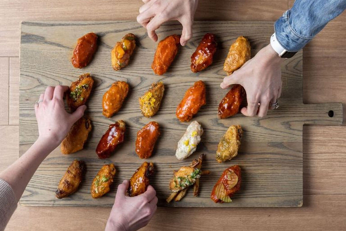 Hands reaching for an assortment of chicken wings