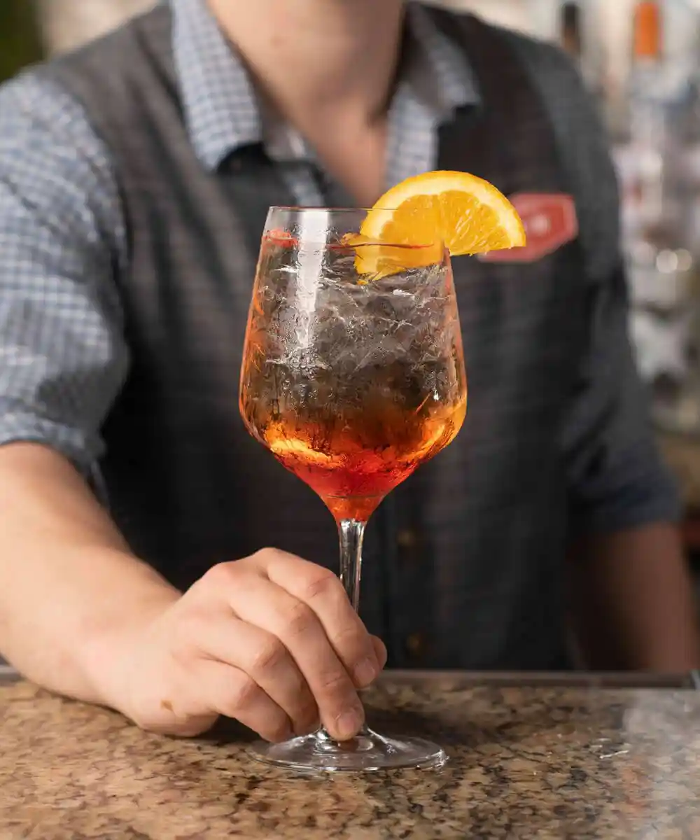 A bartender offering a finished cocktail to the viewer